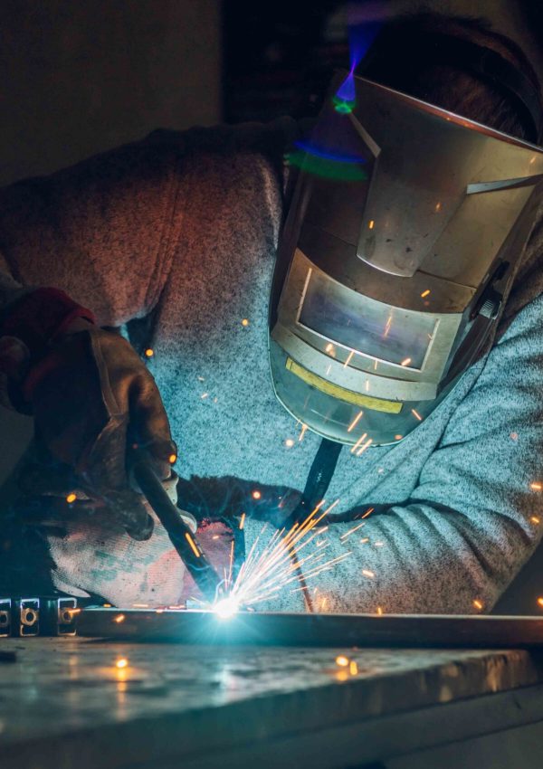 Man worker welding metal with welding machine in a factory or wo Worker in a factory welding metal with welding machine while wearing a protective gear. Yellow sparks fly in sides during working with steel at workshop. Dangerous work concept.